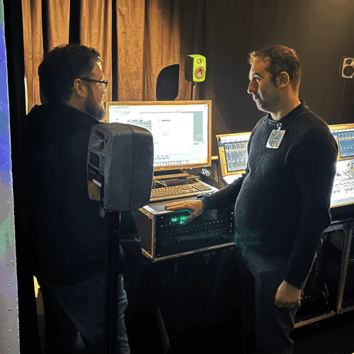 DirectOutin Claudio Scavazza keskustelee messukävijän kanssa. Etualalla ja taustaseinällä Genelec-kaiuttimia.