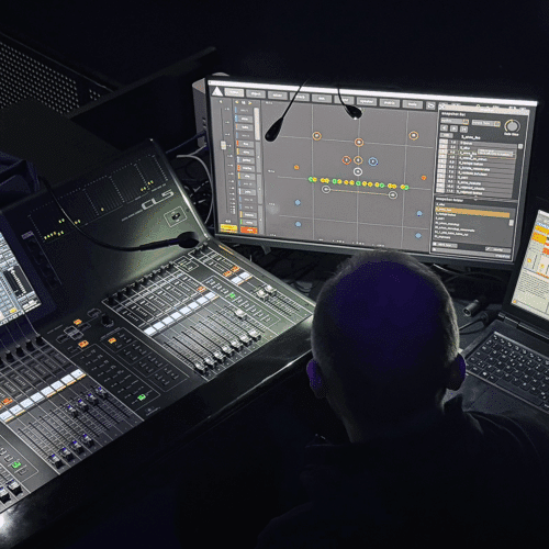 Miksauspiste henkilön pään takaa kuvattuna. Näytöllä FletcherMachinen ohjausnäkymä ja vieressä Yamaha CL5-miksauspöytä.