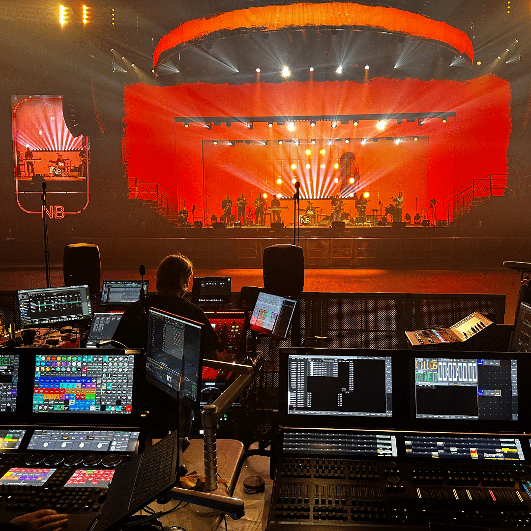 Nylon Beatin bändi tekemässä soundcheckiä taustascreenien oranssissa valossa. Etualalla ääni- ja valopöytiä sekä salimiksaaja.