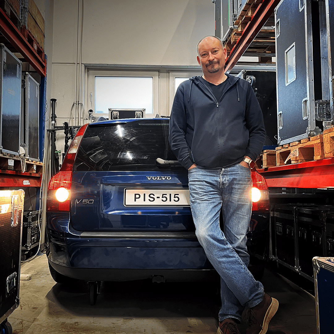 Pekka Olava seisoo PIS-515-rekisterikilvellä varustetun sinisen Volvo V50 farmarin takaluukun edessä varastossaan.